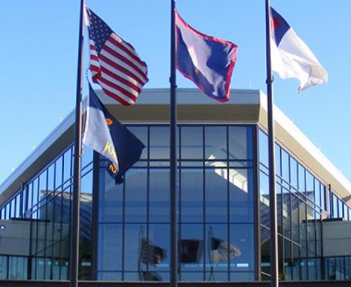 En el centro de la bandera de Guam está su escudo de armas, un emblema en la forma de almendra que representa un vela proa navegando en Agana Bay y GUAM en letras rojas. La forma del emblema recuerda las piedras de lanza utilizadas por los ancestros de los isleños. La forma de relieve en la parte de atrás representa el despeñadero Punta Dos Amantes en Guam.