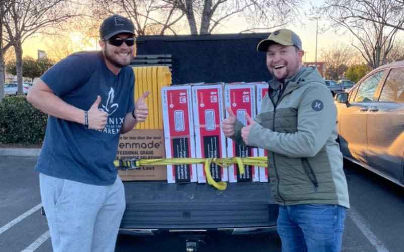 Two men smile in front of a pickup truck.