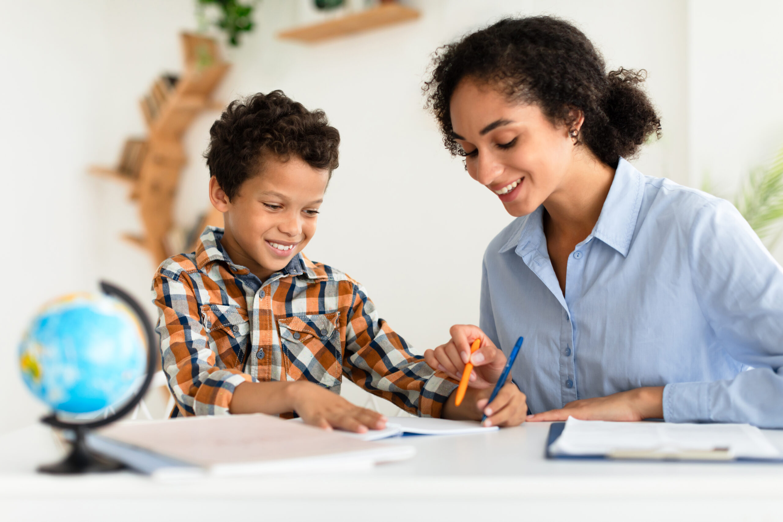 Tutor Lady Teaching School Boy Sitting At Desk Indoors